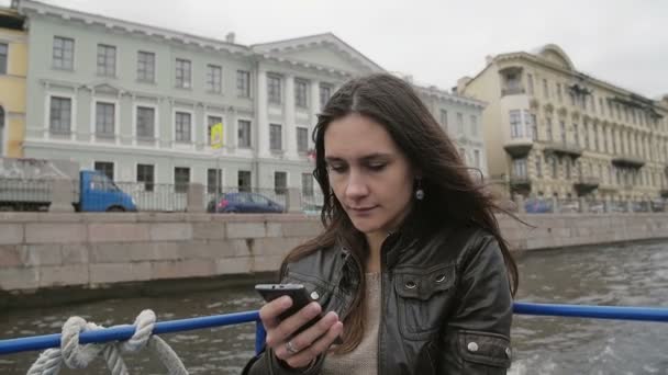 Mulher morena bonita em um passeio pelo rio admirando a vista da cidade. Mulher passear em São Petersburgo usando smarthone slow mo — Vídeo de Stock