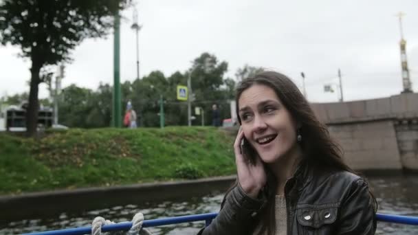 Una giovane donna parla al telefono durante un tour sul fiume. Felice bella ragazza visite turistiche. Il vento le sta soffiando i capelli. Lento mo — Video Stock
