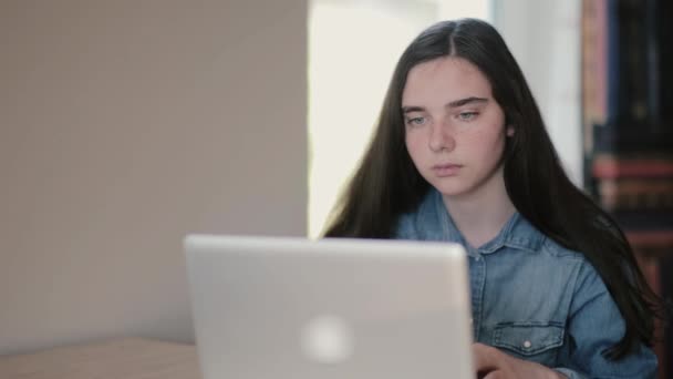 Retrato de uma adolescente estudante usando um laptop navegando na Internet enquanto se senta na mesa em casa — Vídeo de Stock