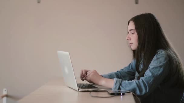Πορτρέτο ενός φοιτητή έφηβο κορίτσι χρησιμοποιώντας ένα φορητό υπολογιστή στο Διαδίκτυο ενώ κάθεστε στο τραπέζι στο σπίτι — Αρχείο Βίντεο