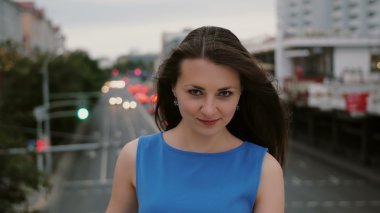 Güzel genç kadın uzun siyah saçlı Rüzgar. mutlu, gülümseyen kız köprüde ayakta ve kameraya benziyor. 4k