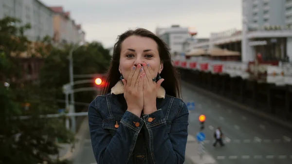 Веселую, счастливую, улыбающуюся девушку, стоящую на мосту, посылающую поцелуи, веселую, смотрящую в камеру. 4K — стоковое фото