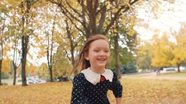 Portret schattig meisje met krullend haar, in jurk met polka dots runing door de herfst steeg in het Park slow mo — Stockvideo