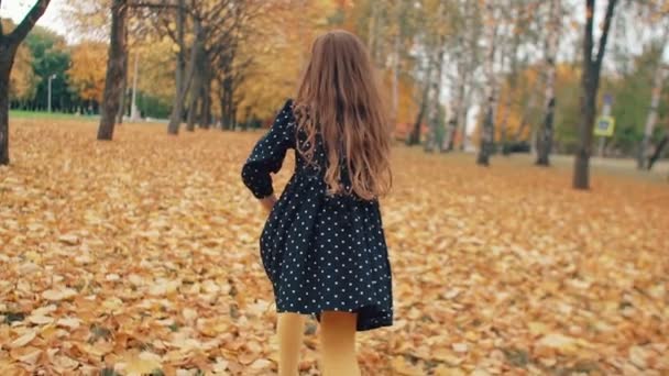 Gelukkig schattig meisje met krullend haar, in jurk met polka dots lopen door de herfst steeg in het Park slow mo — Stockvideo