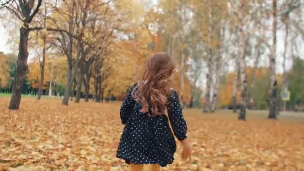 Gelukkig schattig meisje met krullend haar, in jurk met polka dots lopen door de herfst steeg in het Park slow mo — Stockvideo