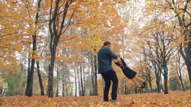 Young handsome father turns his cute little daughter around holding her hand in autumn park slow mo — 图库视频影像