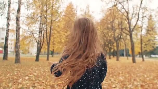 Χαρούμενο χαριτωμένο κοριτσάκι με σγουρά μαλλιά, σε φόρεμα με πουά τρέχει μέσα από το φθινοπωρινό σοκάκι στο πάρκο αργή mo — Αρχείο Βίντεο