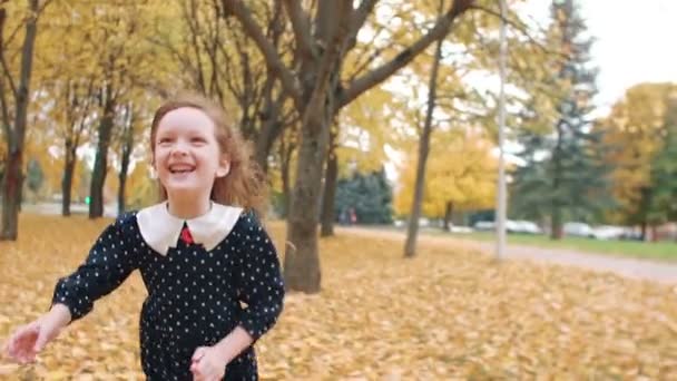 Portret schattig meisje met krullend haar, in jurk met polka dots runing door de herfst steeg in het Park slow mo — Stockvideo