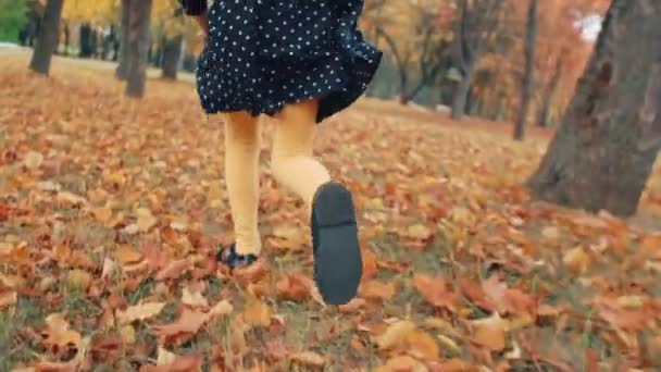 Primer plano linda niña con el pelo rizado, en vestido con lunares corriendo por el callejón de otoño en el parque lento mo — Vídeos de Stock