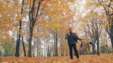 young handsome father turns his cute little daughter around holding her hand in autumn park slow mo