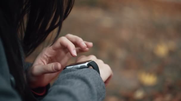 Close-up hermosa, elegante, mujer joven utiliza reloj inteligente sentado en cuadros en el parque de otoño. 4k — Vídeos de Stock