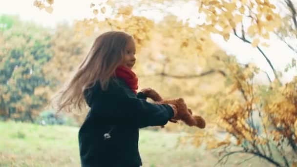 Primer plano divertido alegre linda niña girando con su juguete, oso de peluche amarillo en el increíble parque de otoño cámara lenta — Vídeo de stock