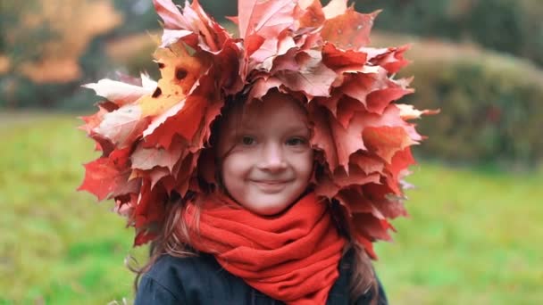 Close-up retrato de feliz sorrindo linda menina bonito em uma coroa coroa de grinalda de folhas de bordo de outono câmera lenta — Vídeo de Stock