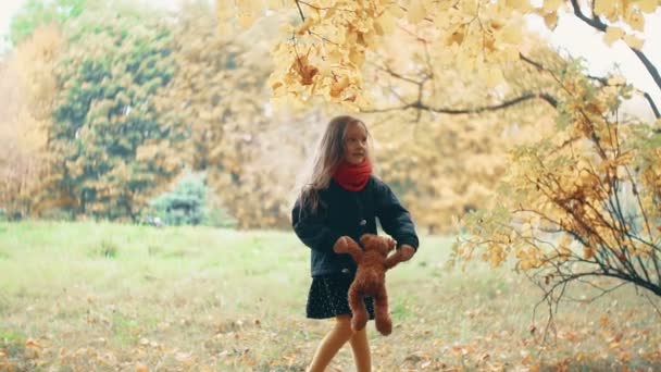 Divertida, alegre linda niña girando con su juguete, oso de peluche amarillo en el increíble parque de otoño cámara lenta — Vídeo de stock