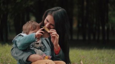 young beautiful mother playing with her cute little son, who is sitting on her lap in the autumn park