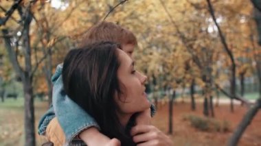 young mother holds on shoulders cute little boy, little boy hugs her near bird feeders in amazing autumn park 4k
