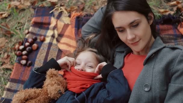 Ibu cantik dengan putri kecilnya yang lucu berbaring di kotak-kotak bermain dengan daun maple di musim gugur taman 4k — Stok Video