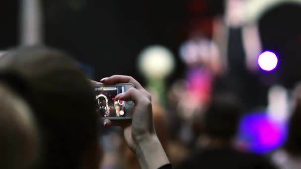 Closeup view of a girl holding smartphone and filming a model during fashion show. — Stock Video