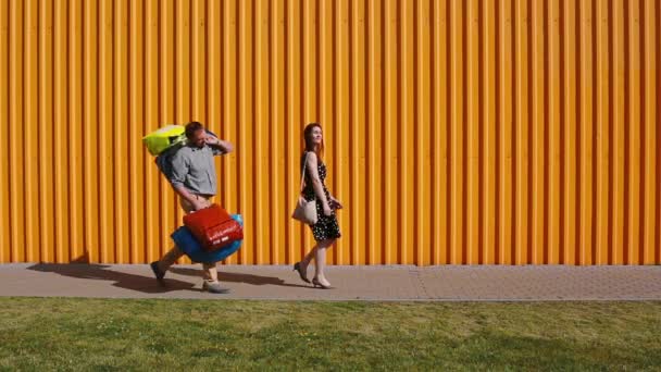 Jovem mulher bonita andando feliz depois de fazer compras. Jovens homens a seguem lutando para levar suas malas . — Vídeo de Stock
