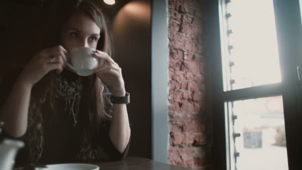 Mujer usando su dispositivo de pantalla táctil smartwatch beber café mirando por la ventana en la cafetería loft 4k — Vídeo de stock