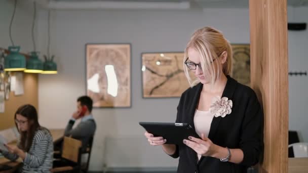 Молодая красивая блондинка-бизнесвумен пользуется планшетом с сенсорным экраном в современном офисе стартапа. Медленный, устойчивый снимок — стоковое видео