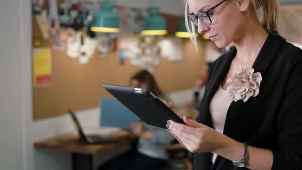 Beautiful blonde business woman uses a tablet in the modern startup office team in the workplace Slow mo, steadicam shot — ストック動画