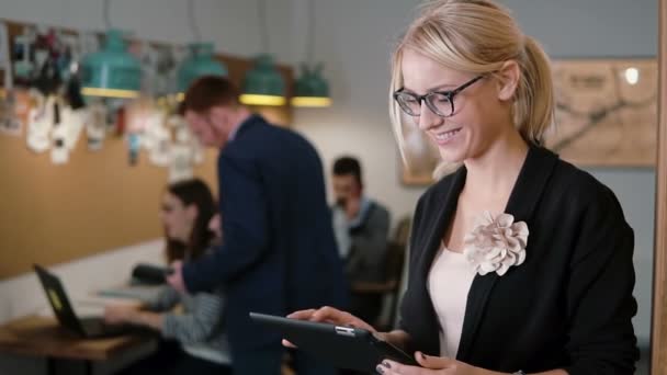 Young beautiful blonde businesswoman uses a touchscreen tablet in the modern startup office. Slow mo, steadicam shot — ストック動画