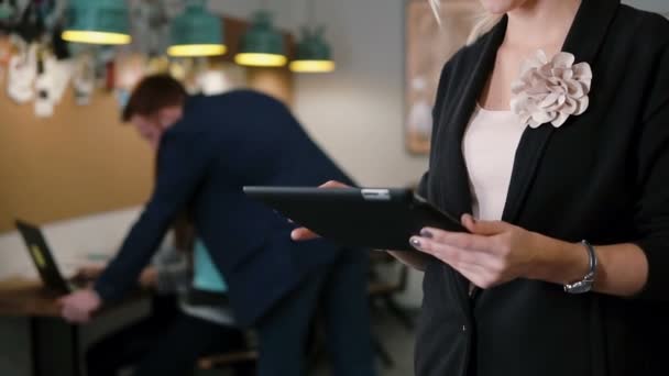 Closeup beautiful blonde business woman uses tablet in modern startup office team in workplace Slow mo, steadicam shot — Αρχείο Βίντεο