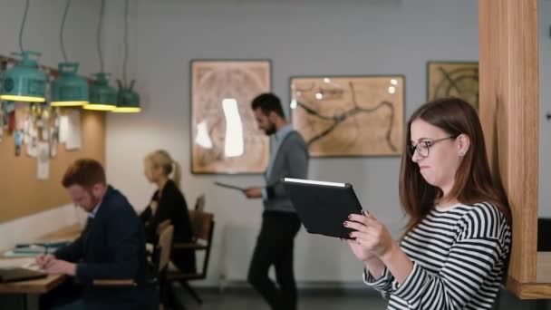 Young attractive brunette woman uses a touchscreen tablet in the modern startup office. Slow mo, steadicam shot — Αρχείο Βίντεο