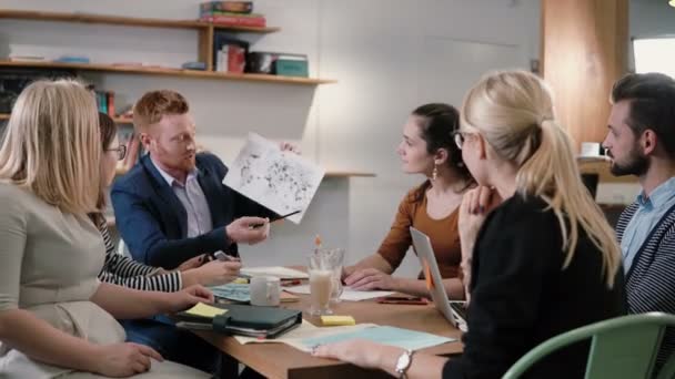 Δημιουργική επιχειρηματική ομάδα στο τραπέζι σε ένα γραφείο σύγχρονου εκκίνησης. Αρσενικό ηγέτης εξηγεί τις λεπτομέρειες του έργου. — Αρχείο Βίντεο