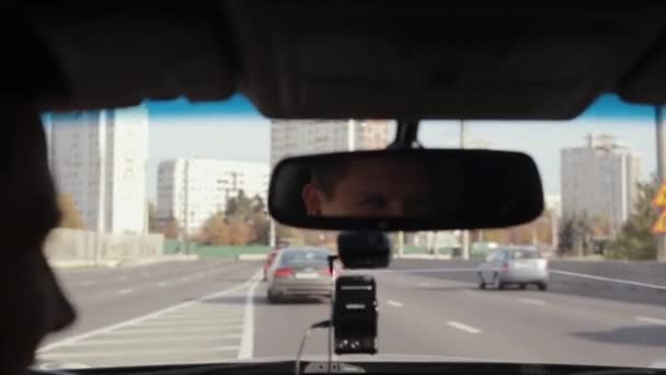 Hombre sonriente en un espejo mientras conduce un coche en una ciudad. Cara de hombre guapo. Viajar en coche . — Vídeos de Stock