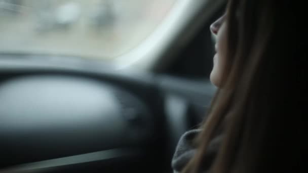 Hezká dívka sedí v autě. Ona drží ruku ovladače a dívá na něj a v okně. Boční a zadní pohled — Stock video