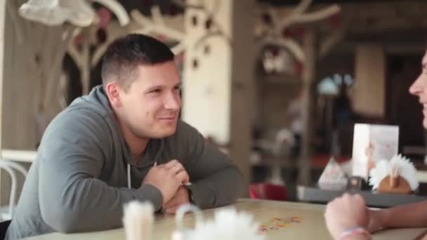 Hombre sonriente hablando alegremente con mujer. Los amantes tienen conversación mientras se sientan en algún lugar con buen diseño de interiores . — Vídeos de Stock