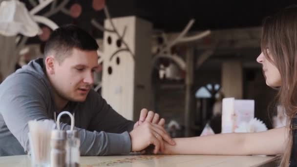 Joven hermosa pareja sentarse en la cafetería y tener una conversación. Se toman de la mano y se miran. Diseño interior acogedor . — Vídeos de Stock