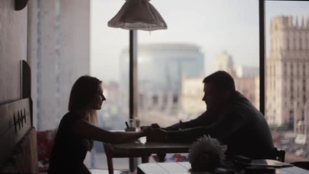 Silhouetten van geliefden op een datum die aan de tafel. Mooi uitzicht op de straat uit raam van café stad op hoge vloer. — Stockvideo
