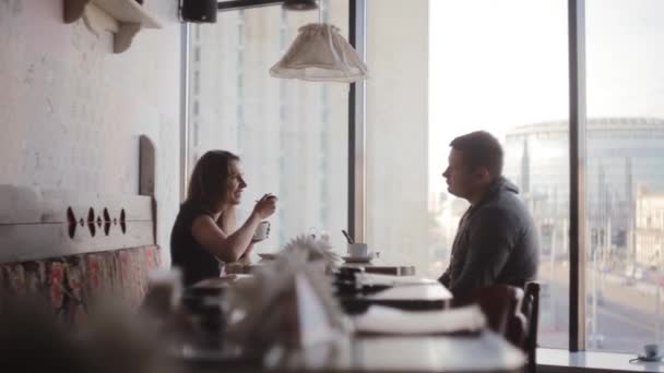 Rest hebben in café. Jonge man en vrouw hebben een maaltijd, praten, lachen. Mooi uitzicht op de stad straat uit raam — Stockvideo