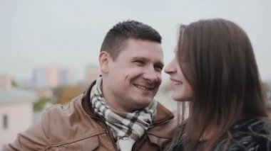 Güzel çift birlikte vakit bir çatı üzerinde. Gülüyorlar, konuşmak ve iyi eğlenceler. Arka planda şehir mimarisi.
