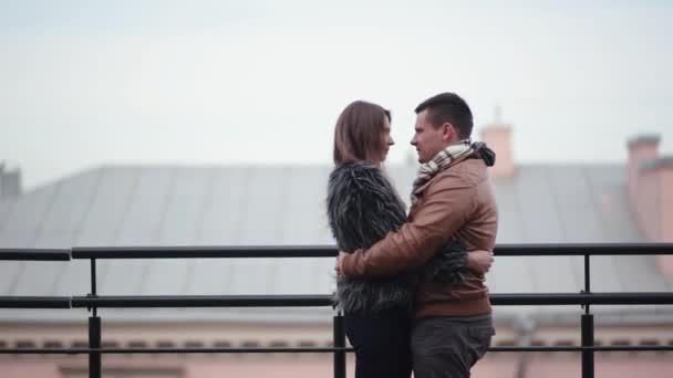 Liebespaar küsst und lacht bei kaltem Wetter auf einem Dach stehend. sie umarmen sich, Mädchen im Pelzmantel, Seitenansicht — Stockvideo