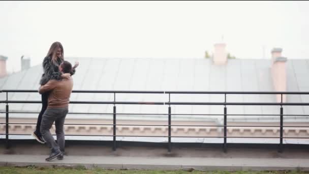 Man lifts his beloved in his arms and swirls around on a roof. Happy lovers have fun together in cold weather — Stock Video