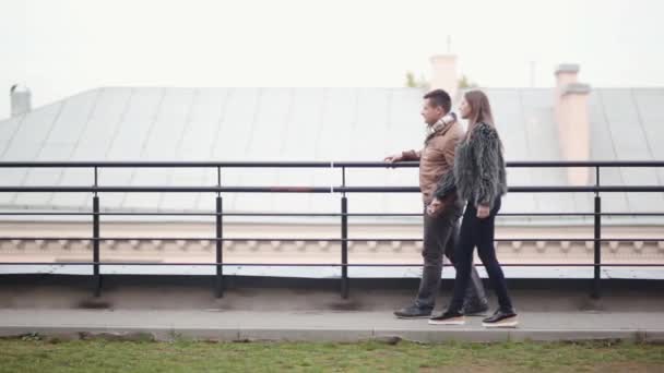 Vista lateral de una feliz pareja paseando por un tejado de una casa en una ciudad. Morena hombre y mujer enamorados . — Vídeos de Stock