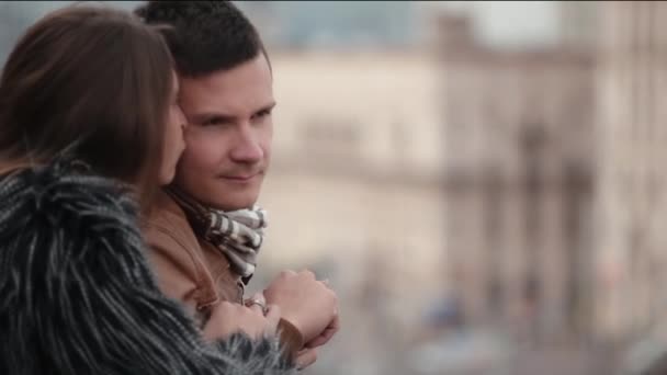 Brunette man en vrouw praat staande op een dak of een balkon. Focus verschuift naar een drukke straat in een stad. — Stockvideo