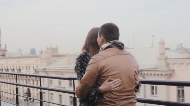 Junger hübscher Mann und verliebte Frau auf dem Dach eines Hauses reden und umarmen sich. eine schöne Aussicht auf Gebäude. Steadicam-Aufnahme — Stockvideo