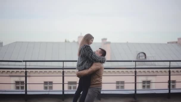 Amor en la ciudad. El hombre feliz levanta a su amada en sus brazos y gira alrededor de un techo. La mujer sonríe alegremente . — Vídeo de stock