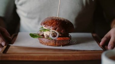 Lezzetli burger bir ahşap tepsi üzerinde çok güzel. Bir adam ellerini alır ve yemek için gidiyordu.