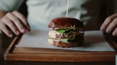 Lezzetli burger bir ahşap tepsi üzerinde çok güzel. Bir adam ellerini alır ve yemek için gidiyordu.