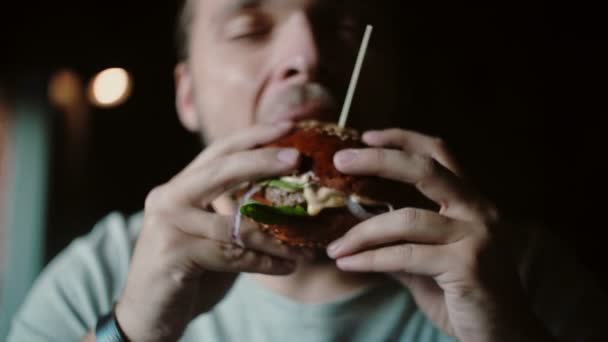 L'uomo si diverte a mangiare, assaggiando la deliziosa carne grande hamburger con formaggio e verdure — Video Stock