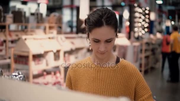 Ελκυστική μελαχρινή κοπέλα στο κατάστημα επιλέγει φωτεινό παιχνίδια διακόσμηση για τα Χριστούγεννα. — Αρχείο Βίντεο