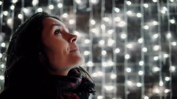 Young attractive woman having fun catches the tongue falling snow at Christmas night, lights at background — Stock Video