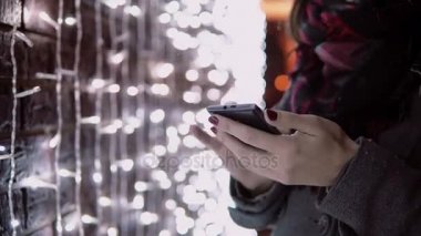yakın çekim eller genç kadın Noel gece ayakta ışıklar duvarının yakınında, düşen kar Smartphone kullanarak,