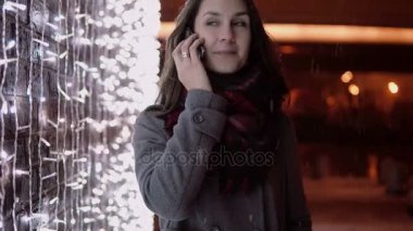 genç çekici kadın Noel gece ayakta ışıklar duvarının yakınında, düşen kar yılında telefon söz,